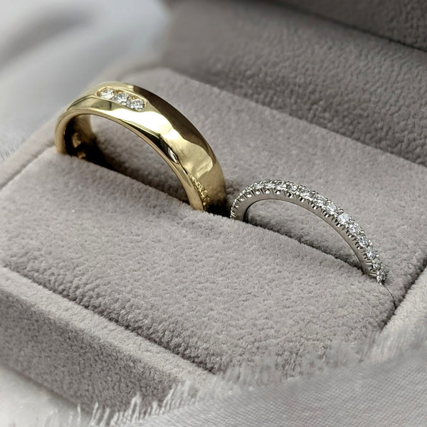 Yellow gold wedding ring with three channel set diamonds, with a platinum and diamond pavé wedding ring sitting on top of it. Both rings are in a gray velvet ring box, with gray ribbon in the foreground.