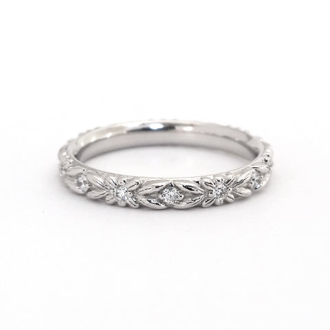 White gold and diamond eternity wedding ring with floral engraving, on a white background.