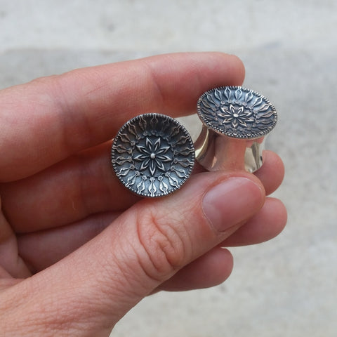 My left hand holding a pair of sterling silver gauge earrings with a botanical engraved pattern.