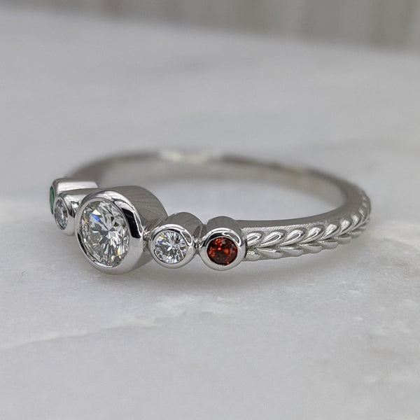Diamond and garnet ring, stones set in bezels, with braid engraving on the shank. The ring is sitting on a pale marble tabletop.
