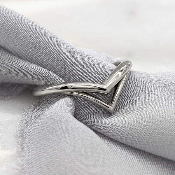 Double chevron wedding ring in white gold with a gray silk ribbon slipped inside it.