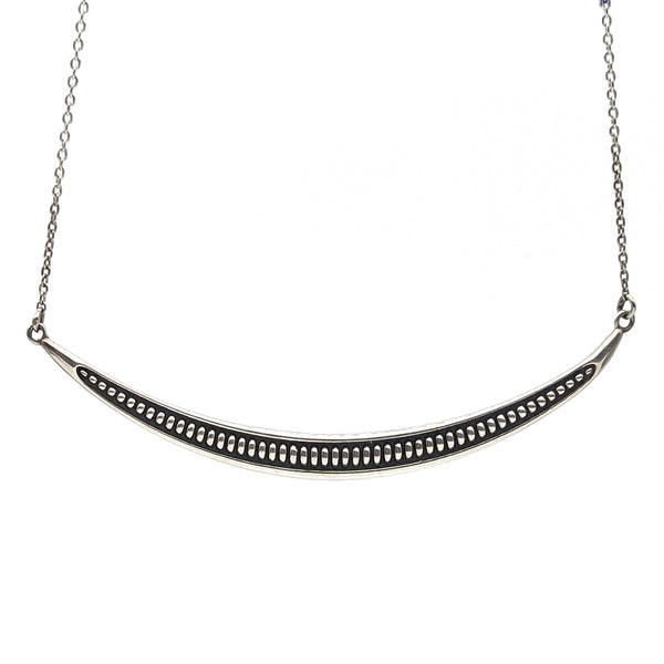 This is a sterling silver arc necklace that has a ribbed texture and a oxidized finish in the background to highlight that texture.