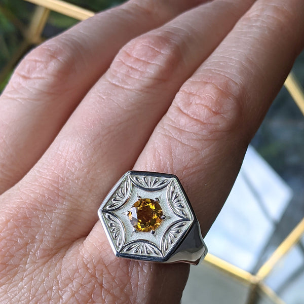 Silver hexagon shaped signet ring with a yellow citrine, worn on the index finger of a woman's hand.