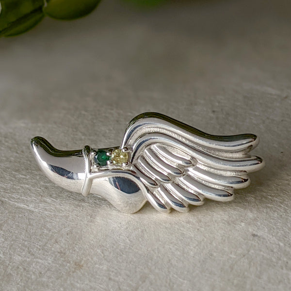 Sterling silver winged shoe tie tack with green and golden gemstones.