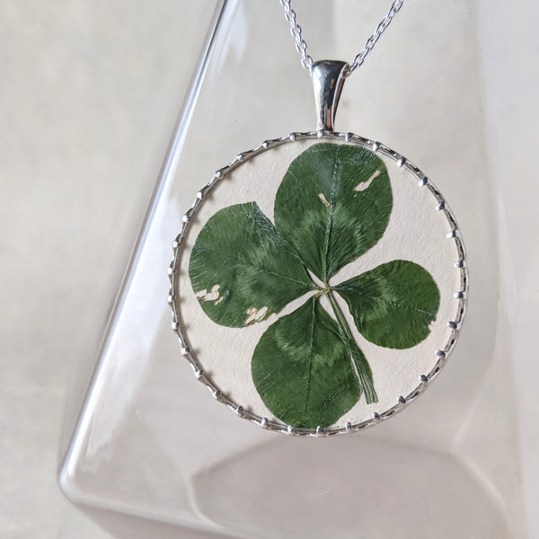 Pressed four leaf clover in a sterling silver and glass pendant. The pendant hangs in front of a clear glass vase.